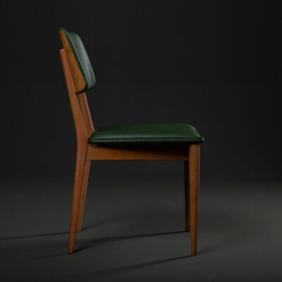 Stylish retro wooden chair with green leather seat in a minimalist studio setting.